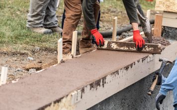 Construction Workers Pouring And Leveling Wet Cement Into Wood Framing.